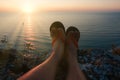 POV view of mans legs in flip-flops on the high cliff in front of setting sun