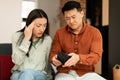 Povertry and debt concept. Unhappy asian spouses having financial problems, looking at empty wallet, sitting on couch Royalty Free Stock Photo