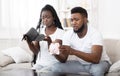 Unhappy afro couple shaking piggybank and wallet at home, searching money Royalty Free Stock Photo