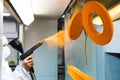 Powder coating of metal parts. A woman in a protective suit sprays powder paint from a gun on metal products