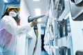 Powder coating of metal parts. A woman in a protective suit sprays white powder paint from a gun on metal products