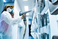 Powder coating of metal parts. A woman in a protective suit sprays white powder paint from a gun on metal products