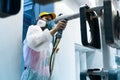 Powder coating of metal parts. A woman in a protective suit sprays white powder paint from a gun on metal products Royalty Free Stock Photo