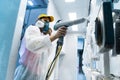 Powder coating of metal parts. A woman in a protective suit sprays white powder paint from a gun on metal products Royalty Free Stock Photo