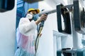 Powder coating of metal parts. A woman in a protective suit sprays white powder paint from a gun on metal products Royalty Free Stock Photo