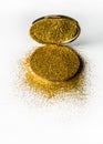 Powder highlighter in a gold powder box with gold sparkles reflected in the mirror. Isolated on white background.