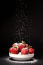 Powdered sugar falls on strawberries in a plate on a black background Royalty Free Stock Photo
