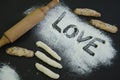 Powdering by flour rolled out dough for bakary stics with wooden rolling pin over black basground. With love Royalty Free Stock Photo