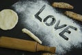 Powdering by flour rolled out dough for bakary stics with wooden rolling pin over black basground. With love Royalty Free Stock Photo