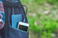 A power bank charges a smartphone in a pocket of a black backpack, on a background of grass