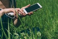 A power bank in the hands of a girl charges a smartphone. against the background of a green field