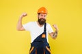 Power building. Strong construction man flex arms yellow background. Bearded man wear hard hat and work uniform