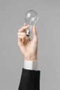 Power consumption and new business idea theme: man's hand in a black suit holding a light bulb on a gray background in studio