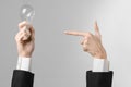 Power consumption and new business idea theme: man's hand in a black suit holding a light bulb on a gray background in studio