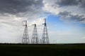 A power line in a field against a cloudy sky with clouds approaching. Power transmission poles high voltage lines on a cloudy day Royalty Free Stock Photo