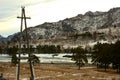 Power line pole on the bank of a beautiful mountain river with snow-covered banks in December Royalty Free Stock Photo