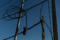 Power lines, electric poles with black straight and twisted wires on bright blue sky