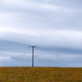 A power lines in a field. Minimalistic landscape, electric post on grass field, cloudy sky