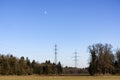 Power lines, steel towers, the moon and blue sky in rural landscape.