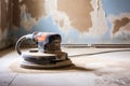 power sander resting on a plastered and sanded wall