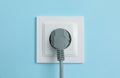 Power socket with inserted plug on light blue wall, closeup. Electrical supply Royalty Free Stock Photo