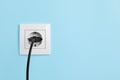 Power socket with inserted plug on light blue wall, space for text. Electrical supply Royalty Free Stock Photo