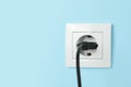 Power socket with inserted plug on light blue wall, space for text. Electrical supply Royalty Free Stock Photo