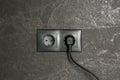 Power sockets with inserted plug on dark grey wall. Electrical supply