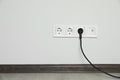 Power sockets with inserted plug on white wall indoors, space for text. Electrical supply Royalty Free Stock Photo