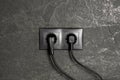 Power sockets with inserted plugs on dark grey wall. Electrical supply