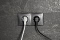 Power sockets with inserted plugs on dark grey wall. Electrical supply