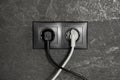 Power sockets with inserted plugs on dark grey wall. Electrical supply