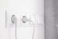 Power sockets with inserted plugs and light switches on white wall indoors Royalty Free Stock Photo