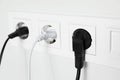 Power sockets with inserted plugs on white wall, closeup. Electrical supply Royalty Free Stock Photo