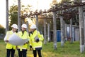 Power specialists are planning a new project outdoors. Three engineers walk near power lines in the high voltage power
