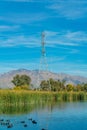 Power or telephone tower used to hang lines with metal exteror in background and tranquil lake with foliage Royalty Free Stock Photo