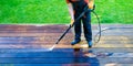 Power washing - man worker cleaning terrace with a power washer - high water pressure cleaner on wooden terrace surface