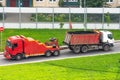 Powerful big red semi evacuation truck tractor tows with attached broken evacuated truck with body driving on city highway