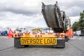 Powerful big rig classic semi truck transporting oversized equipment on step down semi trailer with oversize load sign on the back Royalty Free Stock Photo