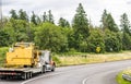 Powerful big rig semi truck with oversized load sign transporting oversize equipment on step down semi trailer running on the Royalty Free Stock Photo