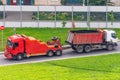 Powerful big rig semi truck tractor tows with attached broken evacuated bulk cargo truck driving on city highway