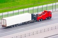 Powerful big rig semi truck tractor tows with attached broken evacuated truck with container trailer driving on city highway,