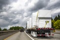 Powerful big rig semi truck tractor transporting heavy duty equipment on flatbed semi trailer driving on the multiline highway Royalty Free Stock Photo