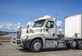 Big rig white day cab semi truck with grille guard transporting cargo in dry van semi trailer running on the road at sunny day Royalty Free Stock Photo