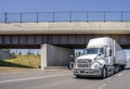 Big rig white semi truck transporting commercial cargo in dry van semi trailer running on the highway road under the bridge Royalty Free Stock Photo