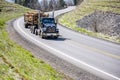 Powerful black day cab big rig semi truck transporting wood logs on the semi trailer running on the winding mountain highway road Royalty Free Stock Photo