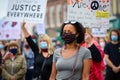 A powerful black female leader wears a Black Lives Matter PPE face mask ahead of other protesters holding signs at a BLM protest