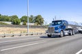 Powerful blue day cab big rig semi truck transporting liquid cargo in shiny tank semi trailer driving on the straight multiline Royalty Free Stock Photo