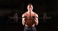 Powerful bodybuilder doing the exercises with barbell. Strong male with naked torso on dark background. Strength and