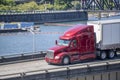Powerful bonnet big rig red semi truck carry cargo in dry van semi trailer running on the overpass road along the river